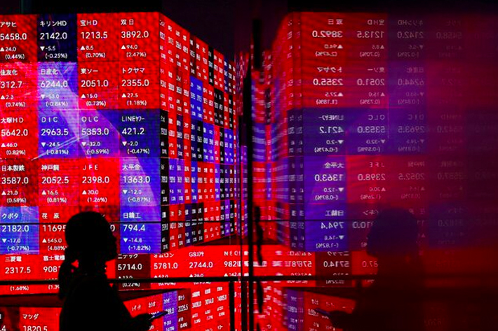 A visitor stands next to an electronic screen displaying Japan's Nikkei stock prices quotation board inside a building in Tokyo