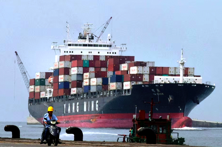 People ride a motorcycle while a container ship passes by at Keelung port in northern Taiwan.