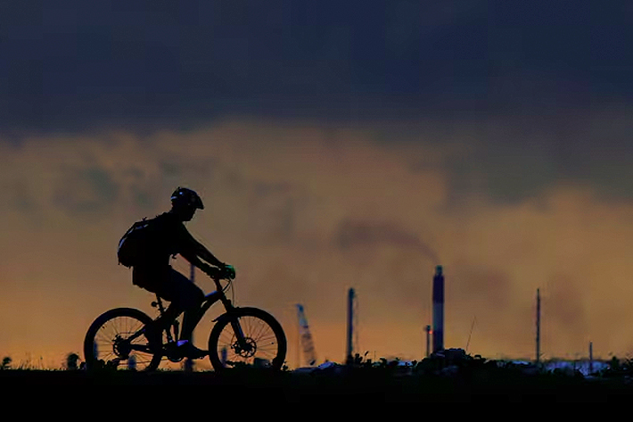 A man cycles past a chimney giving off emissions in an industrial area of Singapore.