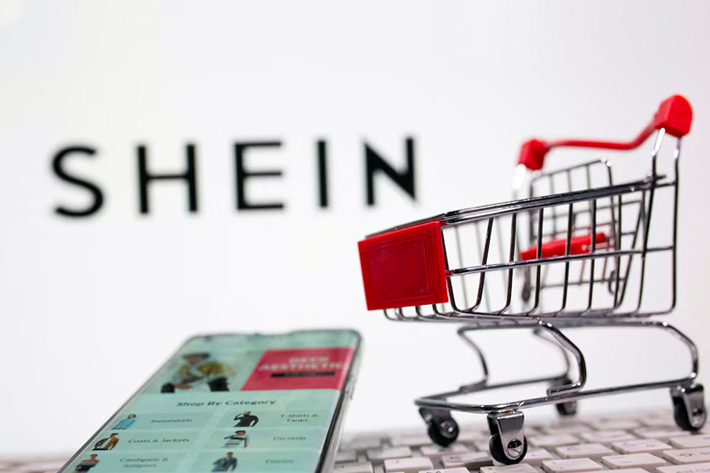 A keyboard and a shopping cart are seen in front of a displayed Shein logo.