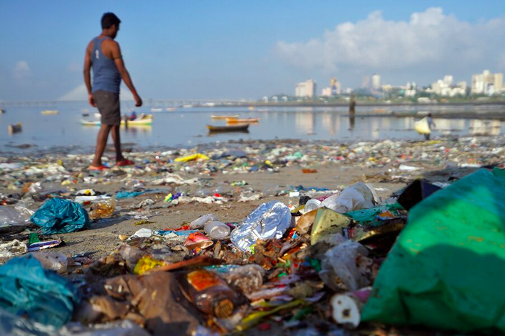 A man walks on a garbage-strewn beach in Mumbai.